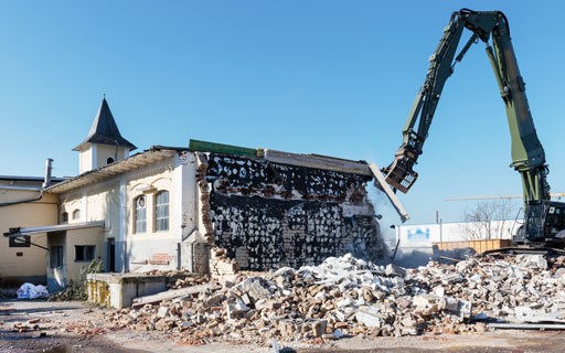 Bagger reißt Gebäude ab, Trümmer auf dem Boden.