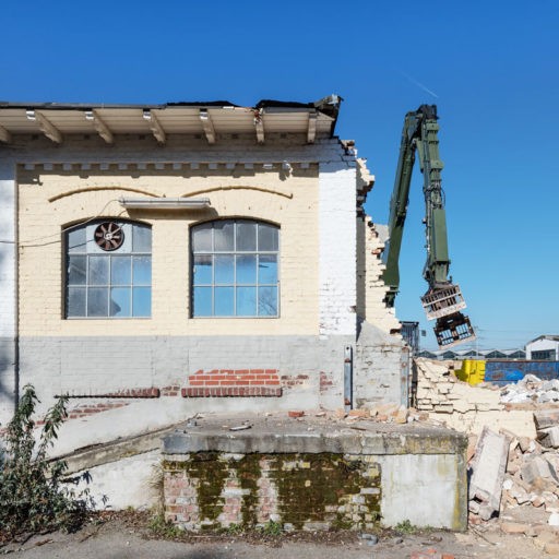 Bagger demoliert altes Fabrikgebäude bei Sonnenschein.